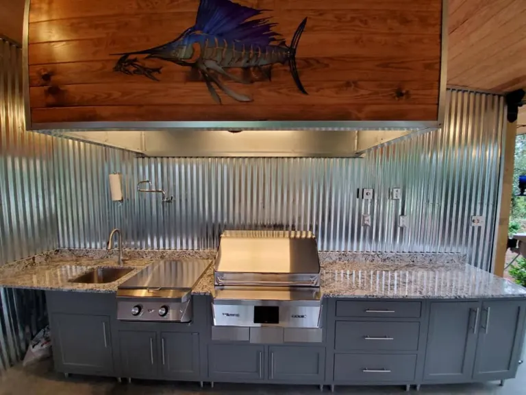 Outdoor kitchen with a stainless grill, stone counter and metal backsplash