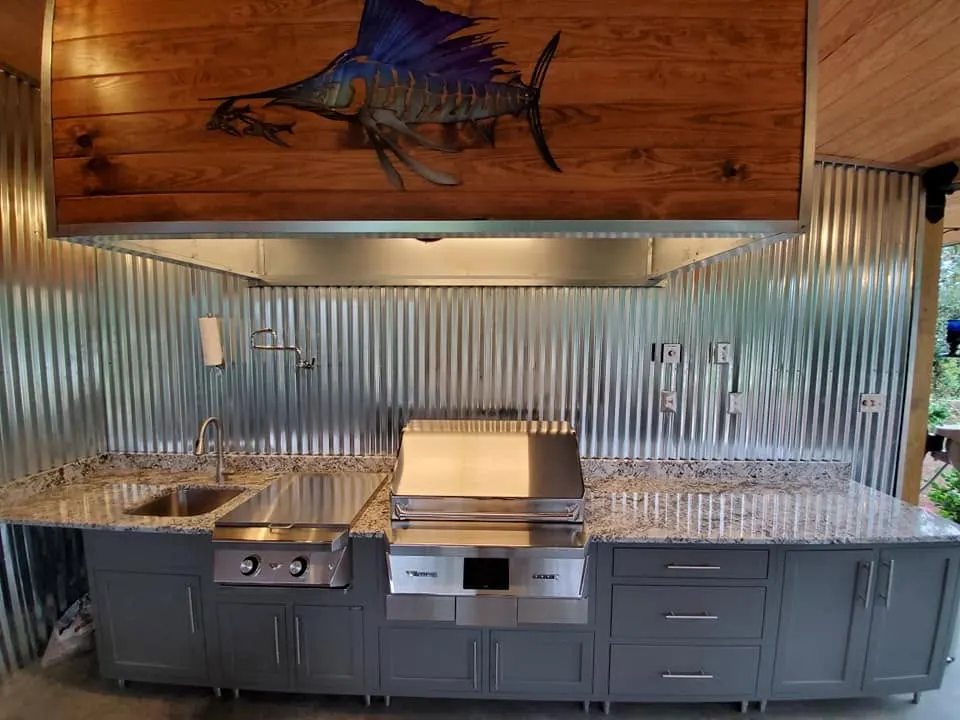 Outdoor kitchen with a stainless grill, stone counter and metal backsplash