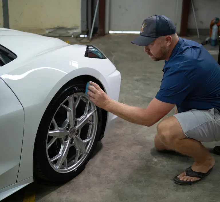 Hand finishing the paint on a white Corvette at the shop
